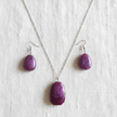 Flat lay of purple stone necklace and matching earrings on white linen