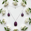 Flat lay of purple stone necklace and earrings with white flowers on white surface