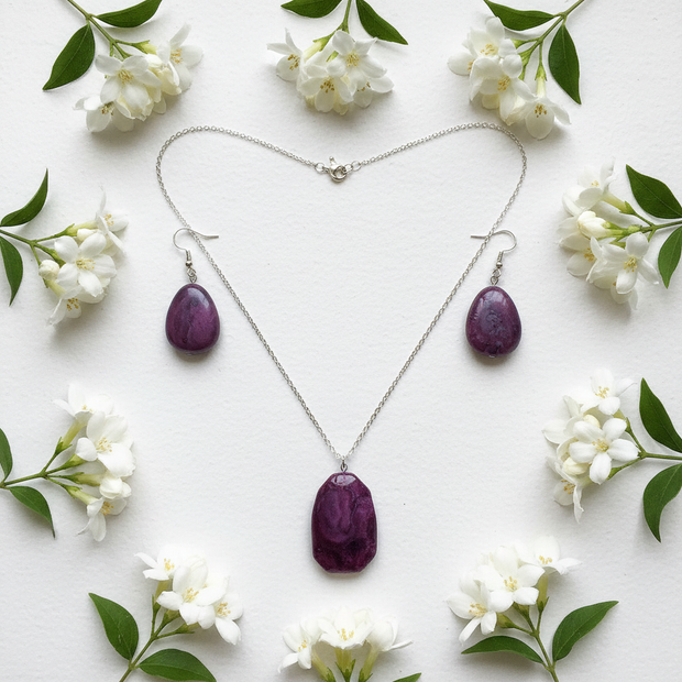 Flat lay of purple stone necklace and earrings with white flowers on white surface