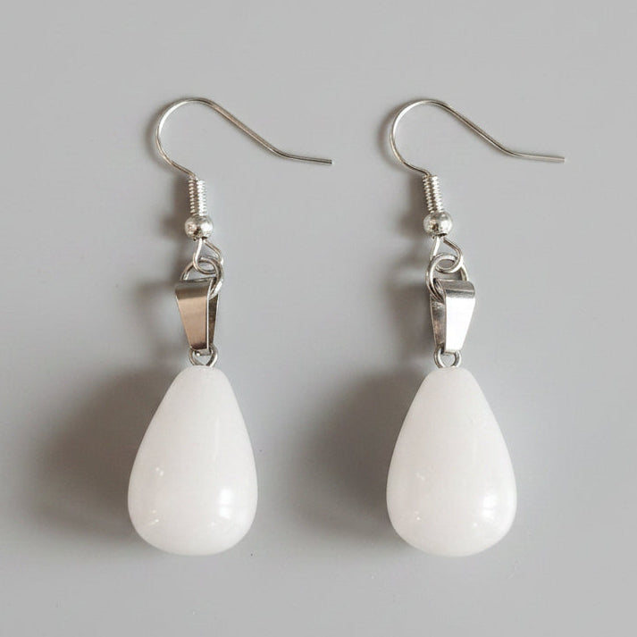 Pair of white teardrop earrings with silver hooks on a gray surface
