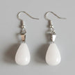 Pair of white teardrop earrings with silver hooks on a gray surface
